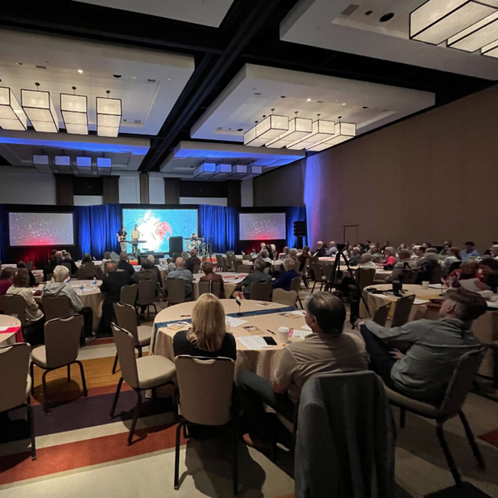 Large audience attending a business presentation in a hotel ballroom.