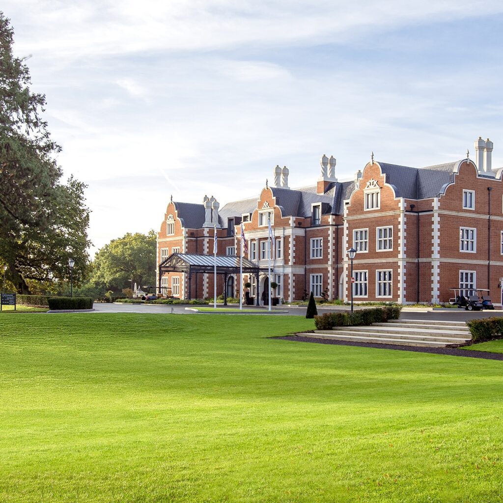 Exterior view of a traditional brick manor house surrounded by green lawns.