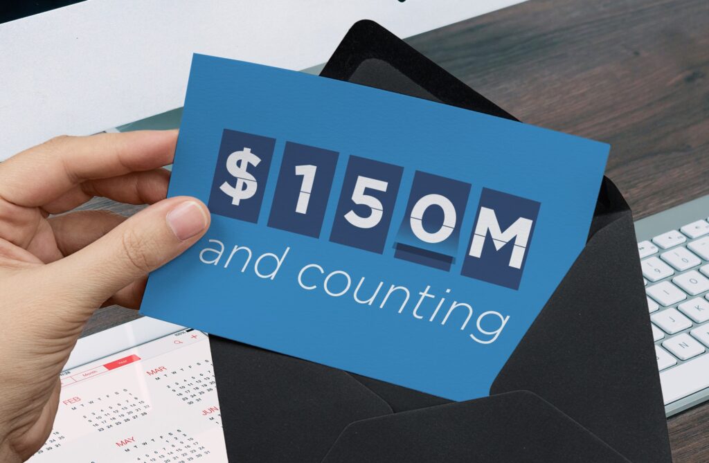 Hand holding a blue card that reads “$150M and counting,” symbolizing fundraising or financial milestone achievement.