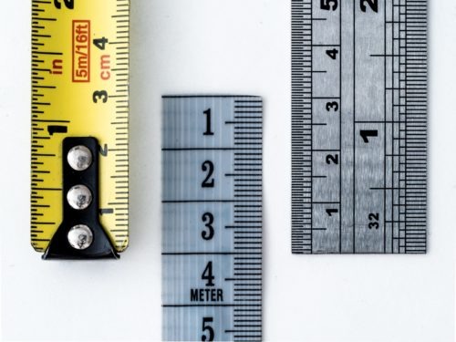 Close-up of measuring tapes and rulers in different styles and units on a white background.